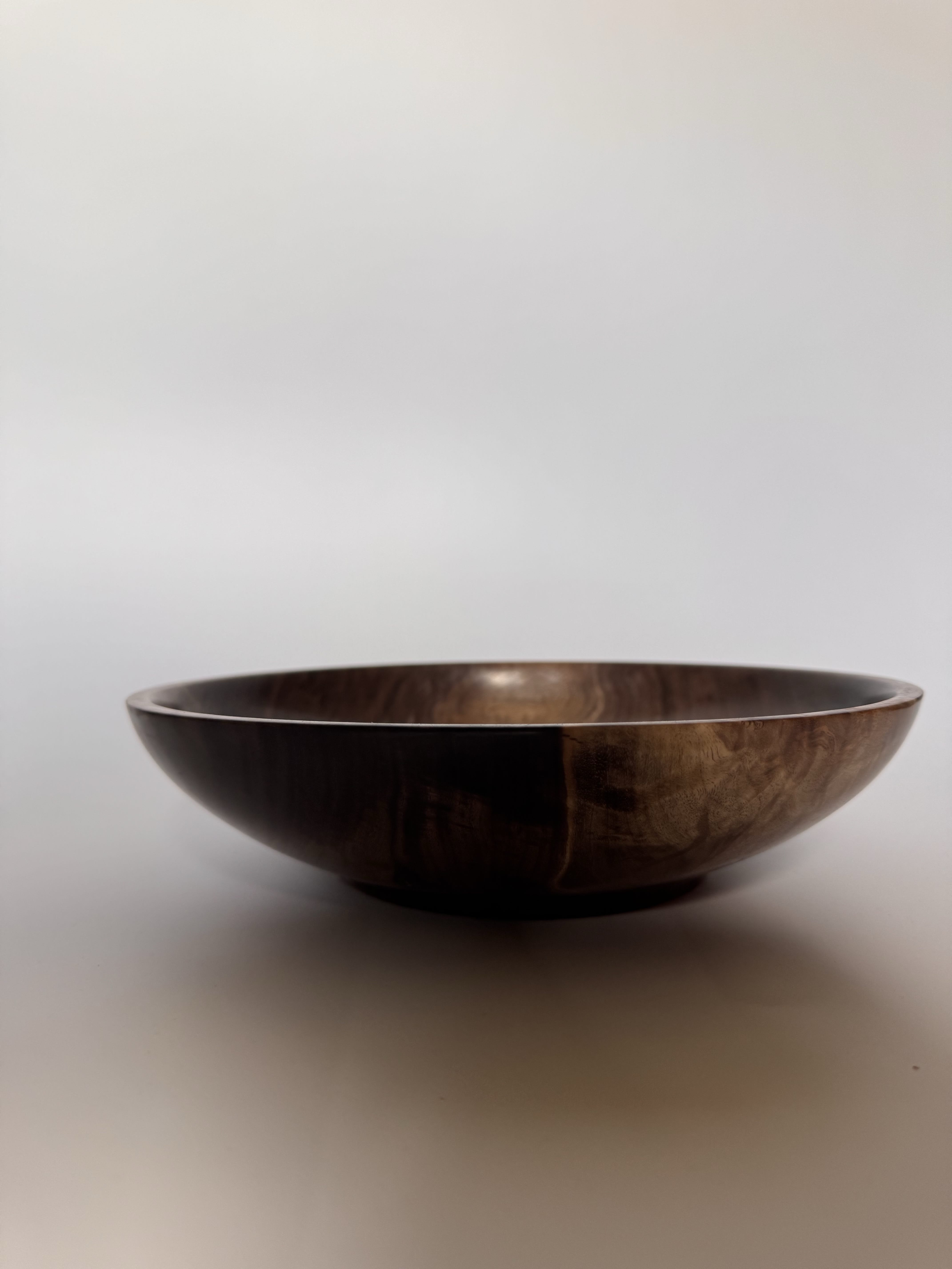 Side profile of hand-turned black walnut bowl with a low open table form